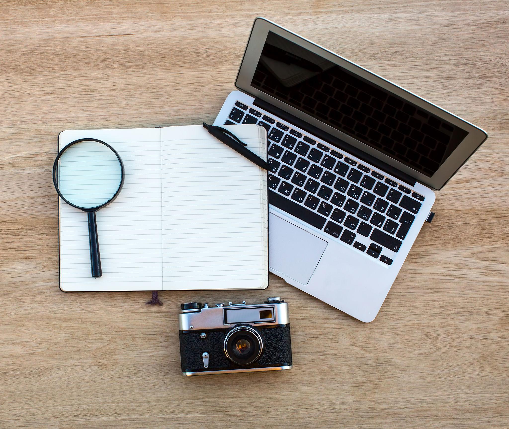 Notebook, magnifying glass, and pen arranged on a research desk.